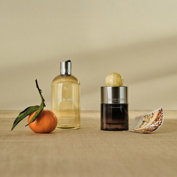 Molton Brown Orange & Bergamot Bath & Shower Gel 300 ml oppfriskende dusjsåpe ved siden av en frisk appelsin og parfyme