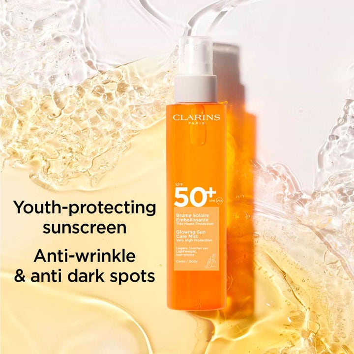 Clarins Glowing Sun Care Mist SPF50+ 150 ml solspray mot rynker i oransje sprayflaske omgitt av gyllent vann
