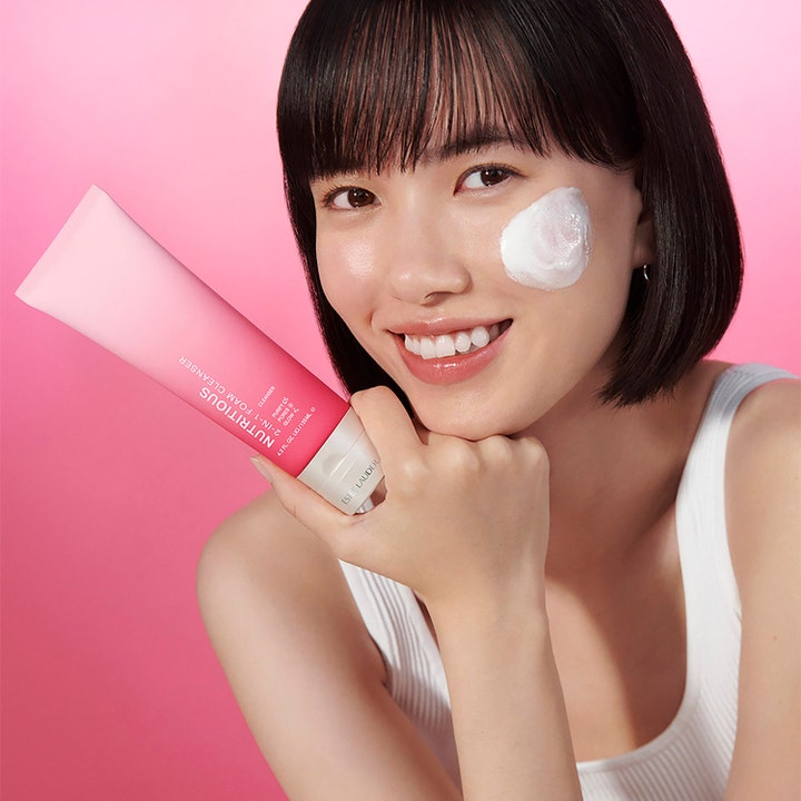 Estée Lauder Nutritious 2-In-1 Foam Cleanser 125 ml ansiktsrengjøring. Modell med hvitt skum på kinnet holder rosa tube.
