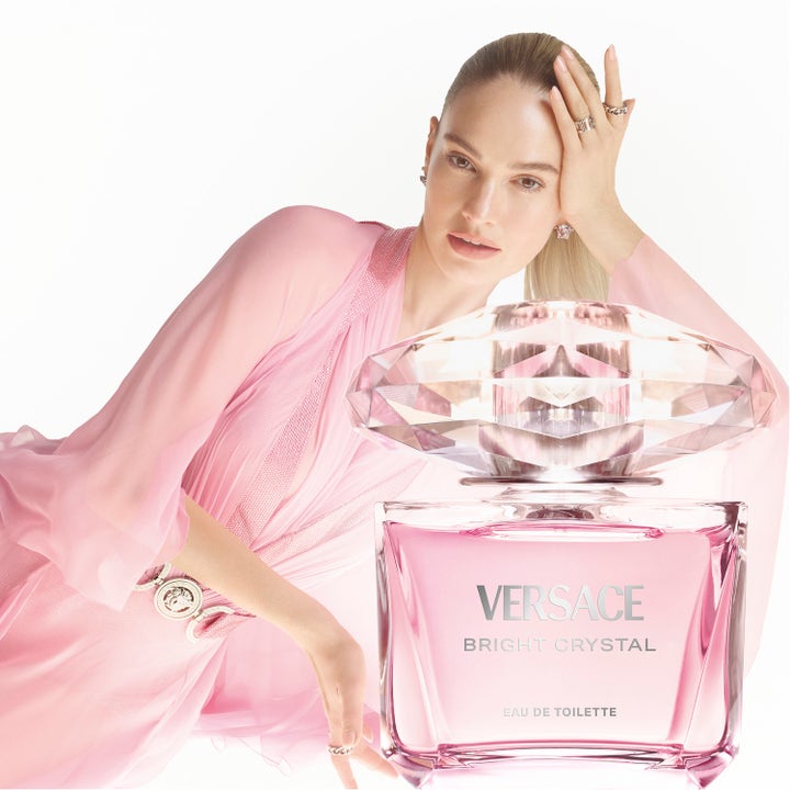 Versace Bright Crystal 200 ml kroppslotion med kvinne i rosa kjole som poserer bak en stor og luksuriøs krystallflaske.