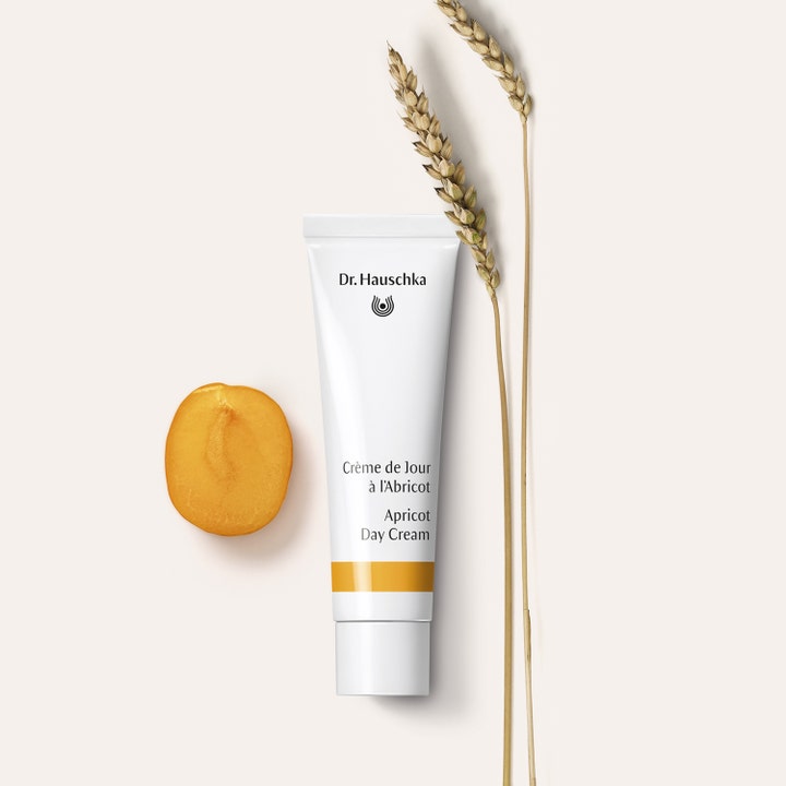 Dr. Hauschka Apricot Day Cream 30 ml glødgivende dagkrem i hvit tube vist med en frisk aprikosskive og tørkede kornaks.