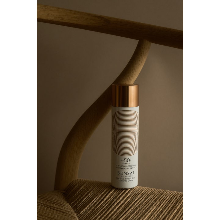 Sensai Silky Bronze Cooling Protective Suncare Spray 150 ml gir SPF50 solbeskyttelse i sprayform vist på en flettet stol.