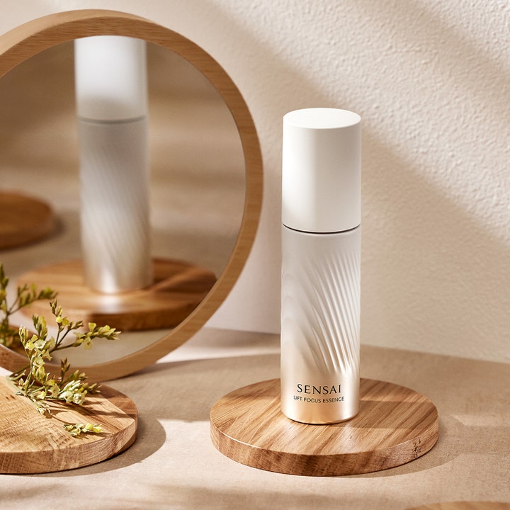 Sensai Lift Focus Essence 40 ml oppstrammende serum i perlemorshvit flaske med tekstur ved et rundt speil.