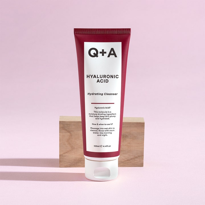Q+A Hyaluronic Acid Gel Cleanser 125 ml fuktighetsgivende ansiktsrengjøring i burgunder tube på en treblokk.