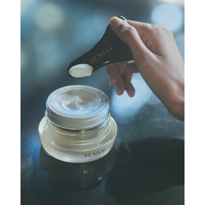 Sensai Ultimate The Mask 75 ml ansiktsmaske viser rik hvit krem på en svart spatel over en elegant glasskrukke