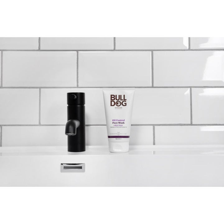 Bulldog Oil Control Face Wash 150 ml renser huden i hvit tube ved en sort kran og hvit flisevegg.