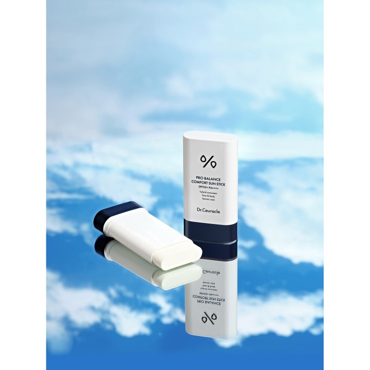 Dr. Ceuracle Pro Balance Sun Stick 18 g solkrem med SPF 50 på en speilflate mot blå himmel og skyer