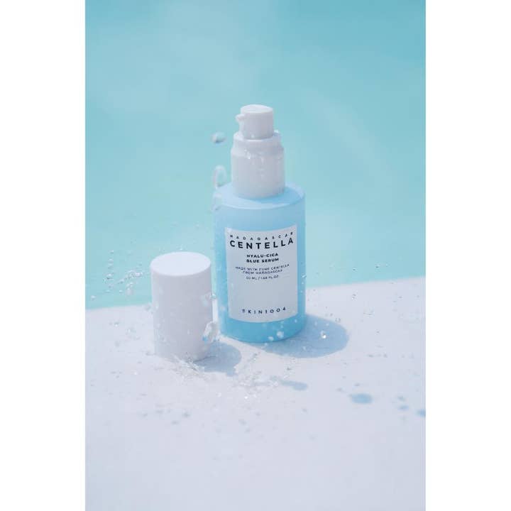 SKIN1004 Madagascar Centella Hyalu-Cica Blue Serum 50 ml beroligende serum i lyseblå pumpeflaske omgitt av vannsprut.