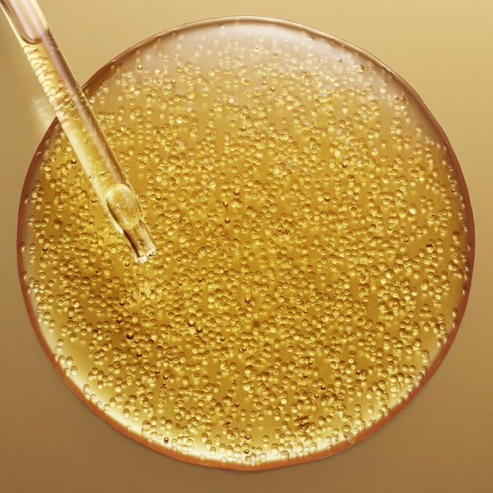 Nuxe Super Serum [10] Eye 15 ml anti-aging øyeserum i gullflaske foran en glitrende bakgrunn av gylne bobler.