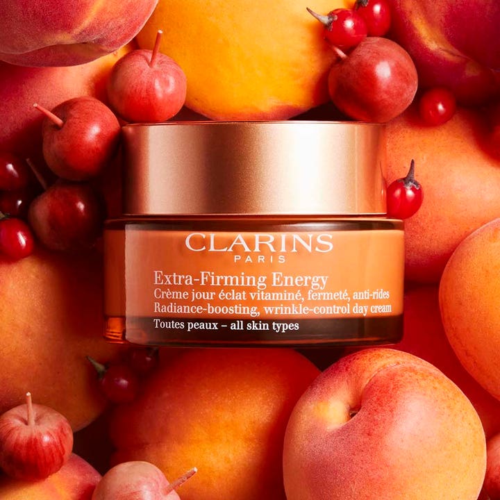 Clarins Extra-Firming Energy 50 ml glødgivende dagkrem i oransje krukke omgitt av friske aprikoser og bær