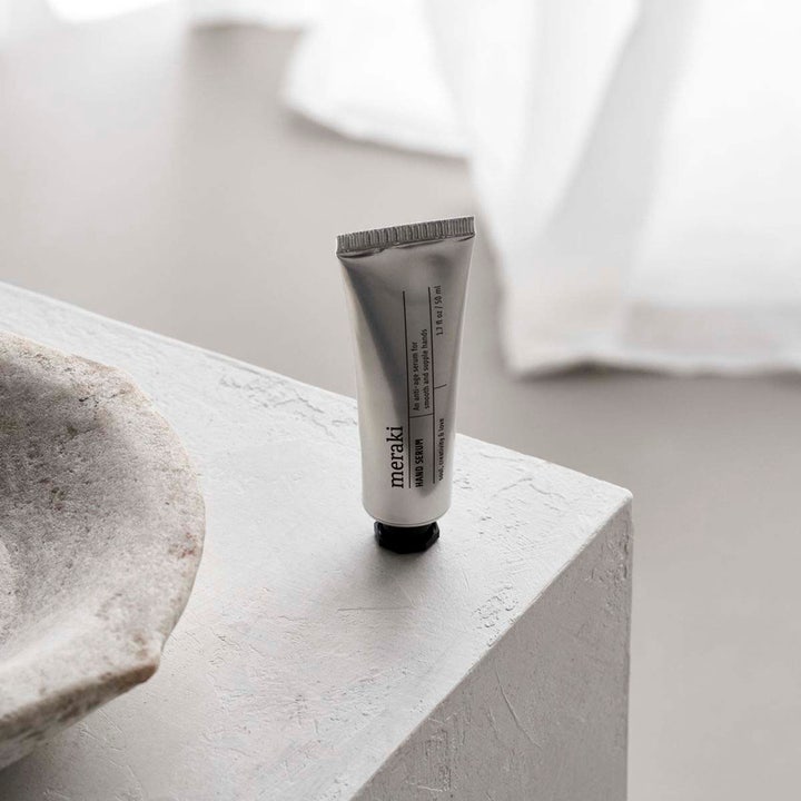 Meraki Hand Serum 50 ml pleiende anti-age håndserum i sølvfarget tube stående på en dekorativ steinflate.