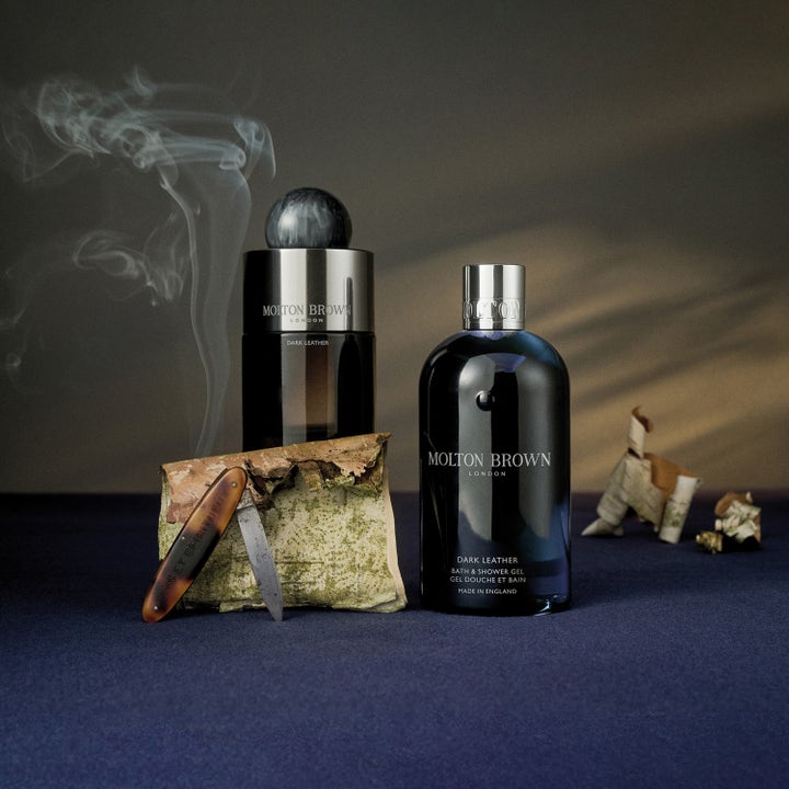 Molton Brown Dark Leather Bath & Shower Gel 300 ml dusjsåpe ved siden av bjørkenever og røyk.
