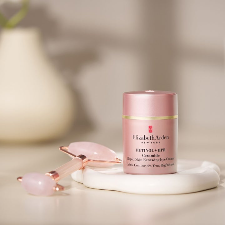 Elizabeth Arden Retinol + HPR Ceramide Eye Cream 15 ml fornyende øyekrem i rosa krukke ved siden av en ansiktsrulle.