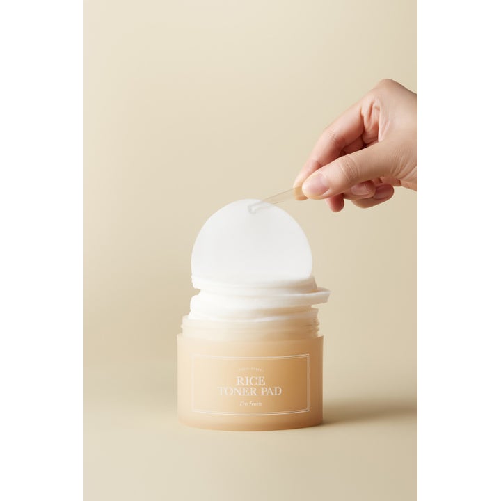 I'm from Rice Toner Pad 60 stk opplysende toner pads i beige krukke der en hvit pad løftes med pinsett.