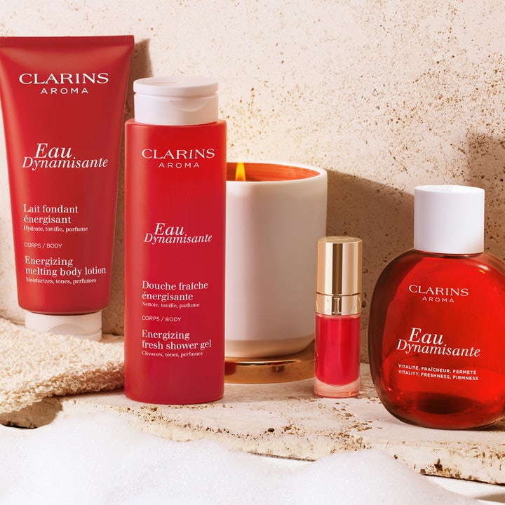 Clarins Eau Dynamisante Energizing Fresh Shower Gel 200 ml oppfriskende dusjsåpe i rød flaske i et lunt miljø med tent lys.