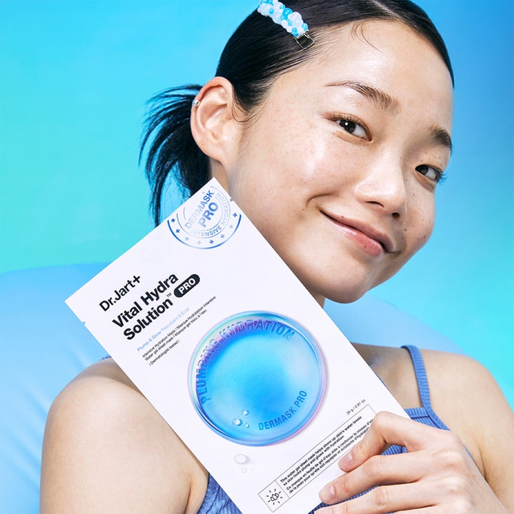 Dr.Jart+ Dermask Vital Hydra Solution Pro 26 g arkmaske holdes av en smilende kvinne mot blå bakgrunn
