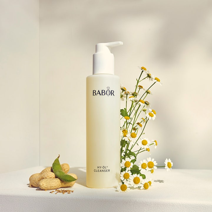 Babor HY-ÖL Cleanser 200 ml ansiktsrengjøring i frostet pumpeflaske omgitt av friske kamilleblomster og peanøtter.