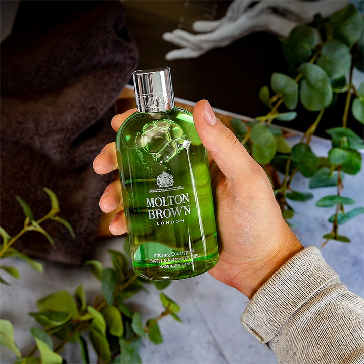 Molton Brown Infusing Eucalyptus Bath & Shower Gel 300 ml oppfriskende dusjsåpe holdes i en hånd med grønne blader
