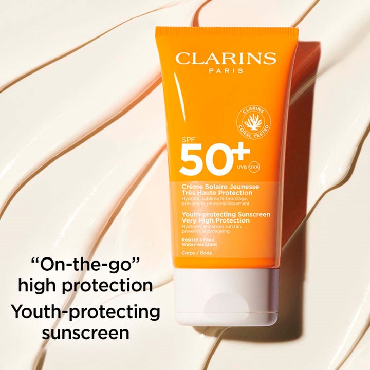 Clarins Youth-protecting Sunscreen 150 ml solkrem spf 50 i oransje tube liggende på kremet tekstur.