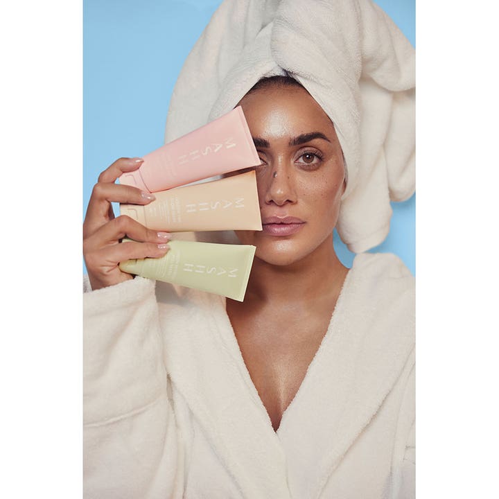 MASHH Golden Tan & Glow Mask 100 ml ansiktsmaske for glød holdes av kvinne i hvit badekåpe og håndkle.