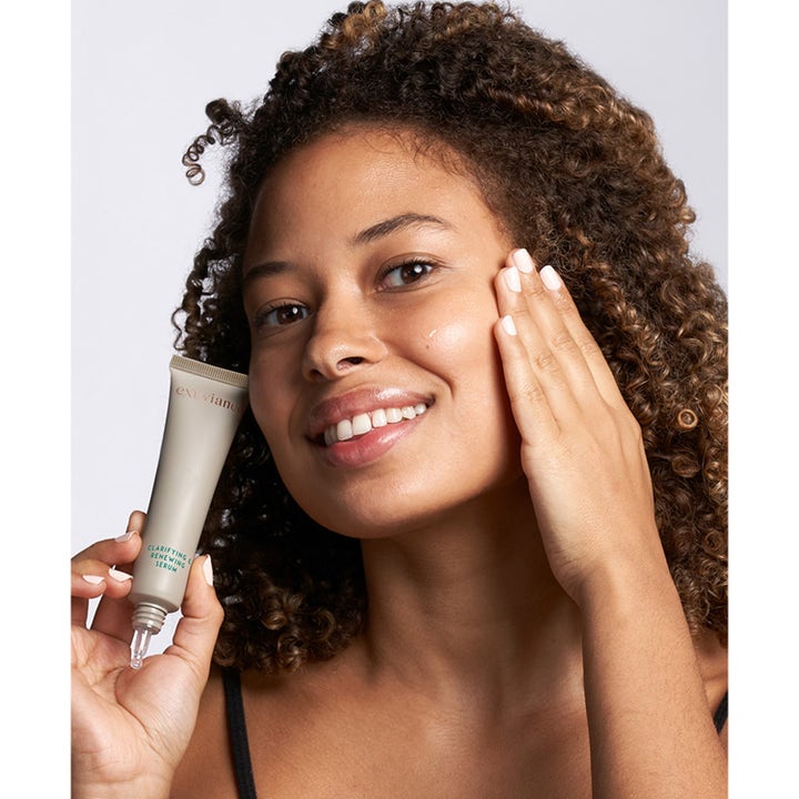 Exuviance Clarifying and Renewing Serum 30 ml klargjørende ansiktsserum i tube holdt av kvinne med en dråpe på kinnet