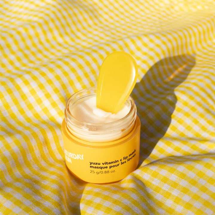 Saturday Skin Yuzu Vitamin C Lip Mask 25 g pleiende leppemaske i gul krukke med hvit krem og spatel på rutete duk