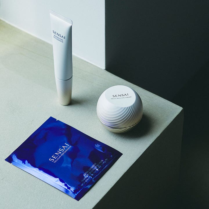 Sensai Total Eye Treatment 35 ml øyepleie med hvit tube, rund krukke og blått brev på en steinoverflate