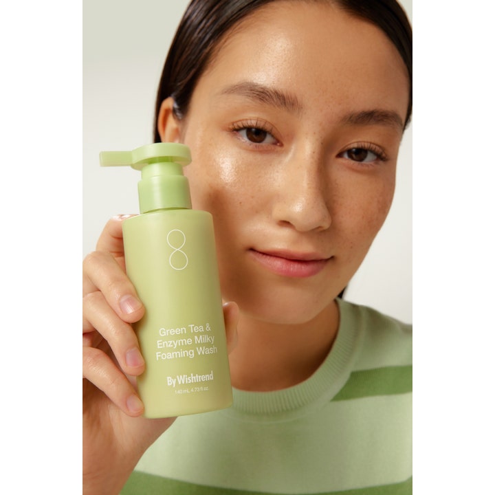 By Wishtrend Green Tea Enzyme Milky Foaming Wash 140 ml ansiktsrens holdes av en ung kvinne med glødende hud
