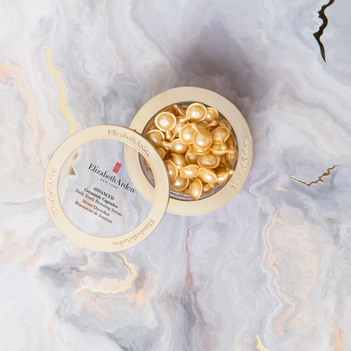 Elizabeth Arden Advanced Ceramide Serum 60 kapsler hudpleie i åpen gullkrukke med gylne kapsler på marmorflate.