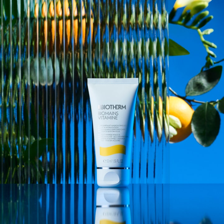 Biotherm Biomains Vitaminé 50 ml fuktighetsgivende håndkrem i hvit tube foran appelsin og blå bakgrunn