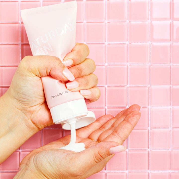 Saturday Skin Rise + Shine Gentle Cleanser 120 ml ansiktsrens klemmes ut av rosa tube i en hånd