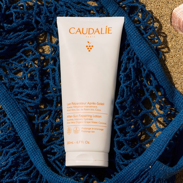 Caudalie Vinosun After-Sun Repairing Lotion 200 ml beroligende aftersun i hvit tube på blått nett og sandstrand