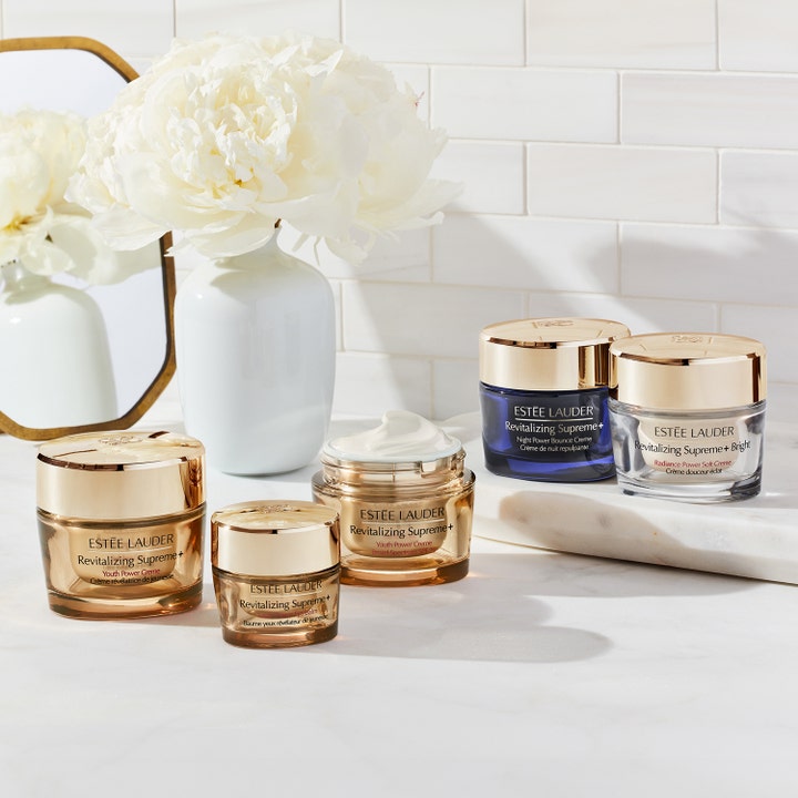 Estée Lauder Revitalizing Supreme+ Bright 50 ml glødgivende ansiktskrem i sølvfarget krukke blant hvite blomster.