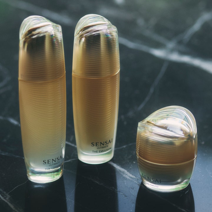 Sensai Ultimate The Cream 40 ml fornyende ansiktskrem i gullfarget krukke sammen med flasker på mørk marmor.