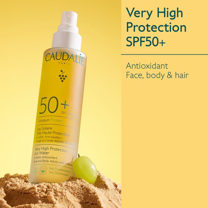 Caudalie Vinosun Very High Protection Water 150 ml solspray med SPF 50+ i gul flaske med grønn drue i sanden.
