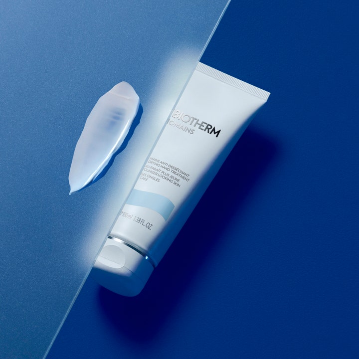 Biotherm Biomains 100 ml fuktighetsgivende håndkrem i hvit tube med en kremet teksturprøve på blå bakgrunn