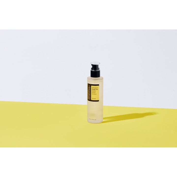 COSRX Advanced Snail 96 Essence 100 ml fuktighetsgivende ansiktsserum med snigelslim i pumpeflaske på gul bakgrunn