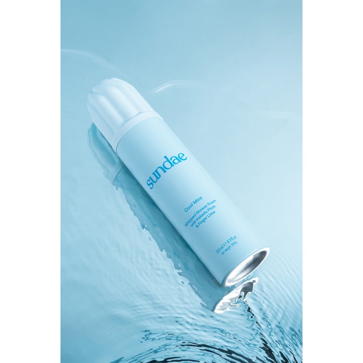 Sundae Whipped Shower Foam Cool Mint 265 ml forfriskende dusjsåpe i lyseblå flaske på en blå vannflate.