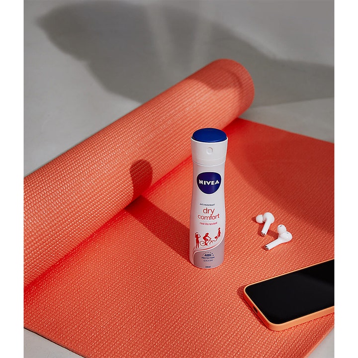 NIVEA Dry Comfort Spray Deospray 150 ml deodorant som gir beskyttelse på en korallfarget yogamatte med ørepropper.