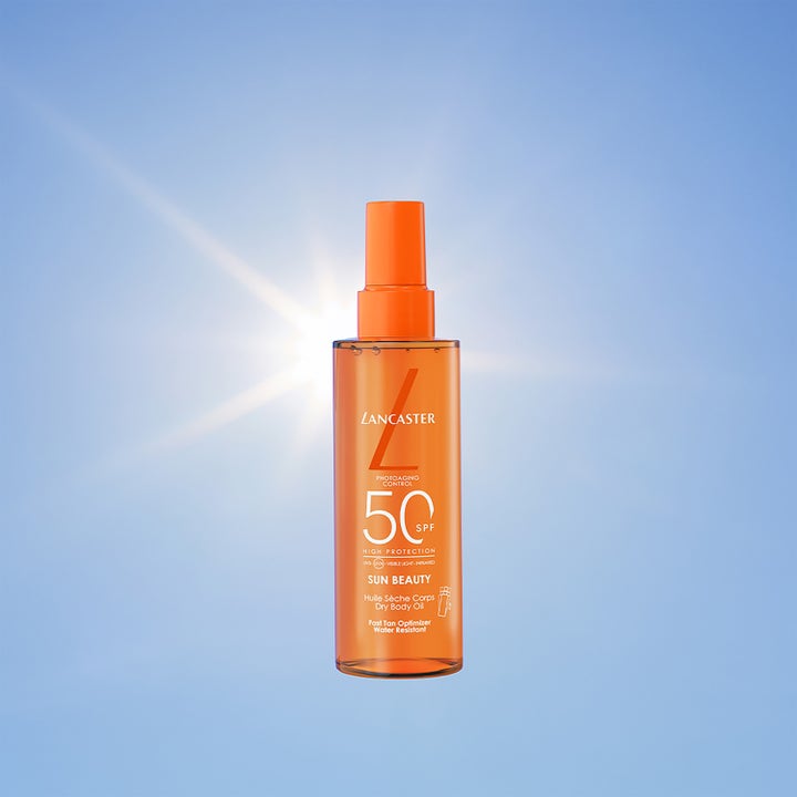 Lancaster Sun Beauty Dry Body Oil 150 ml solbeskyttelse i oransje sprayflaske foran blå himmel og sol