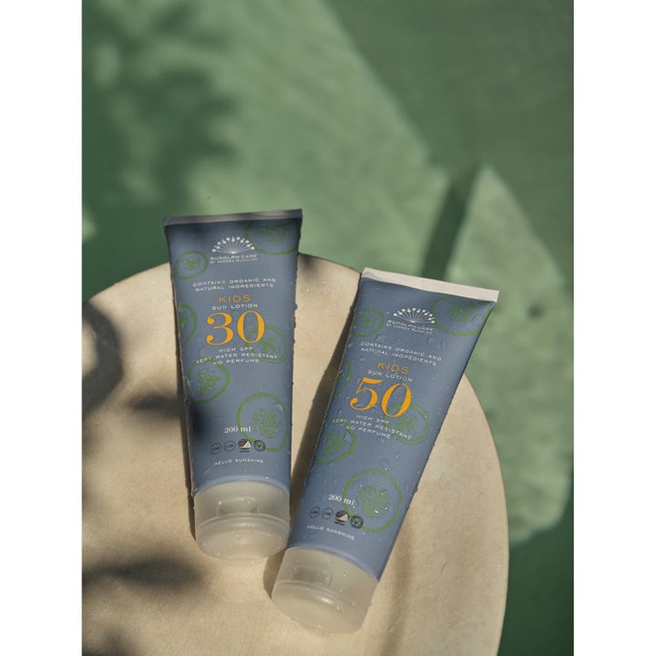 Rudolph Care Sun Lotion Kids SPF50 200 ml vannavstøtende solkrem i blå tuber med vanndråper på en lys steinflate