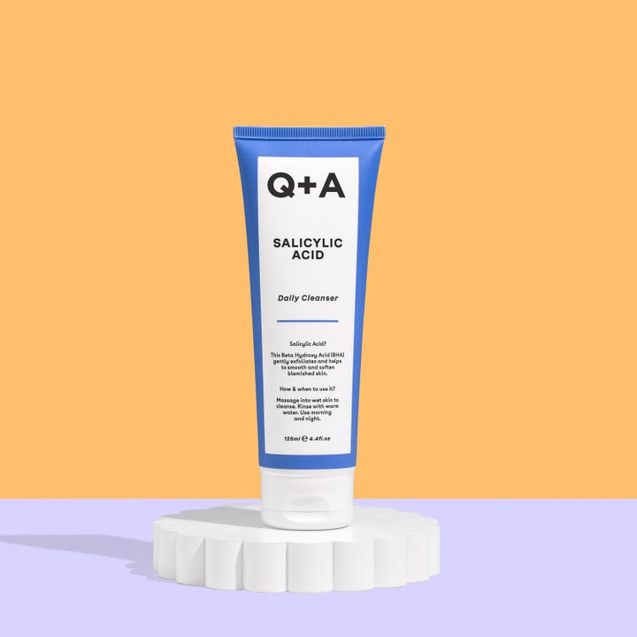 Q+A Salicylic Acid Cleanser 125 ml eksfolierende ansiktsrens i blå tube på en hvit riflet sokkel.