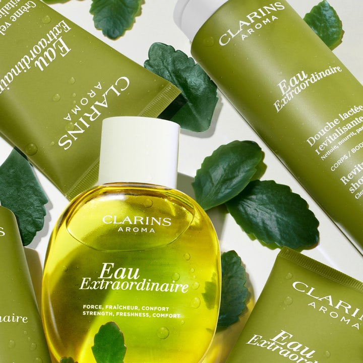 Clarins Eau Extraordinaire Shower Milk 200 ml i grønn tube omgitt av friske blader og gul kroppsolje