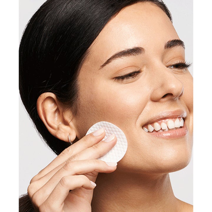 Exuviance Daily Resurfacing Peel 58 ml peeling pads som gir ny glød vist av kvinne som bruker bomullspad på kinnet