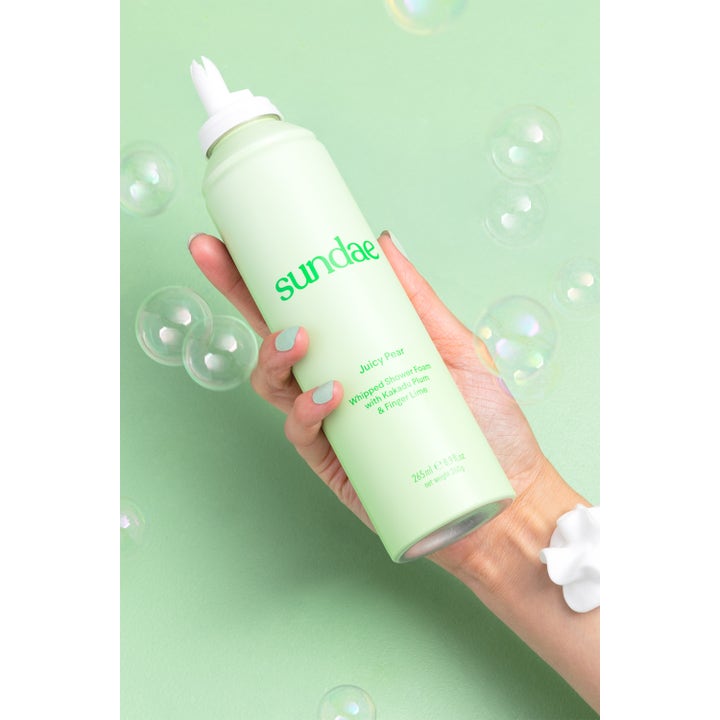 Sundae Whipped Shower Foam Juicy Pear 265 ml dusjsåpe i lysegrønn flaske holdt i en hånd med såpebobler.