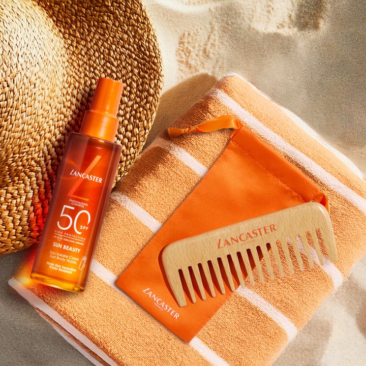 Lancaster Sun Beauty Body Water SPF50 150 ml gir høy beskyttelse i oransje sprayflaske ved en stråhatt på stranden.