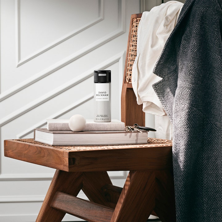 David Beckham Homme Deodorant Spray 150 ml herredeodorant i mønstret flaske plassert på bøker i et stilrent interiør.