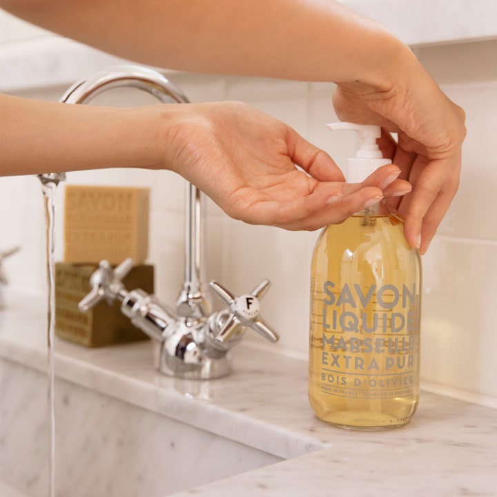 Compagnie de Provence Liquid Marseille Soap Olive Wood 495 ml håndsåpe som pumpes ut i hendene ved en marmorvask.