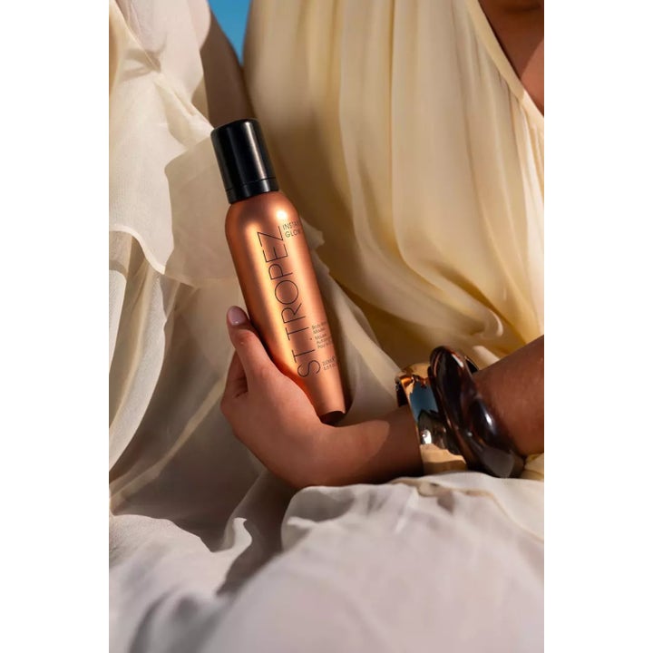 St.Tropez Instant Glow Body Bronzing Mousse 200 ml selvbruning mousse i bronseflaske holdt mot en lys sommerkjole