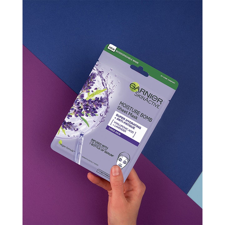 Garnier Skin Active Moisture Bomb 28 g fuktighetsgivende sheetmaske med lavendel holdes mot lilla bakgrunn.